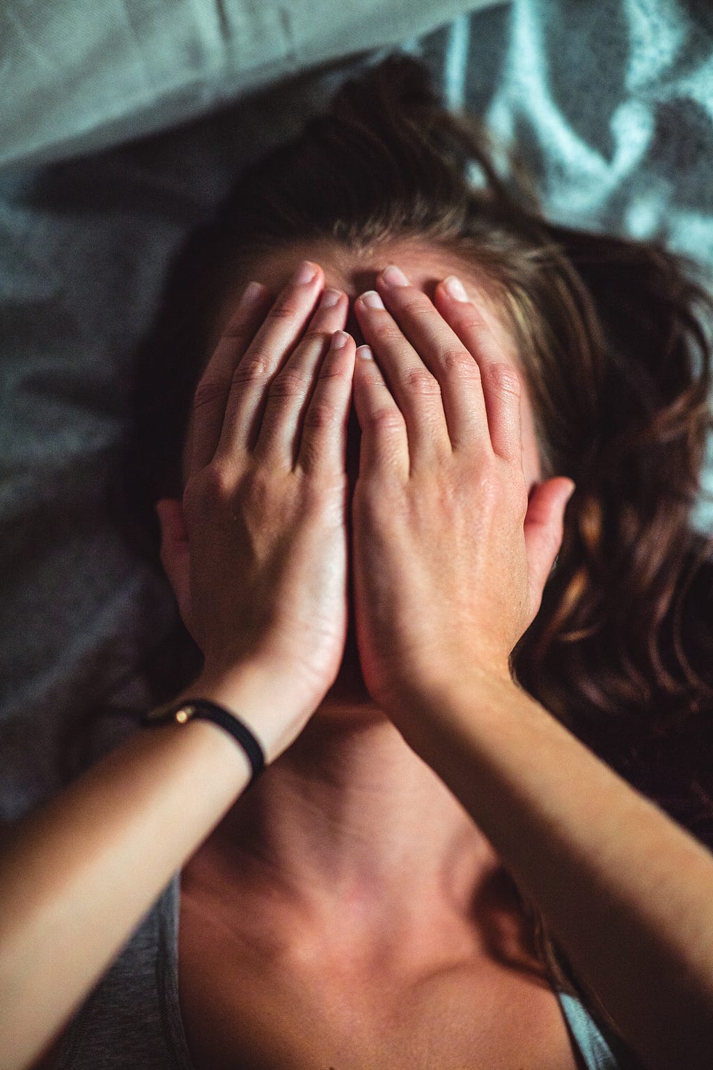 A headshot of a person covering their face with their hands in guilt