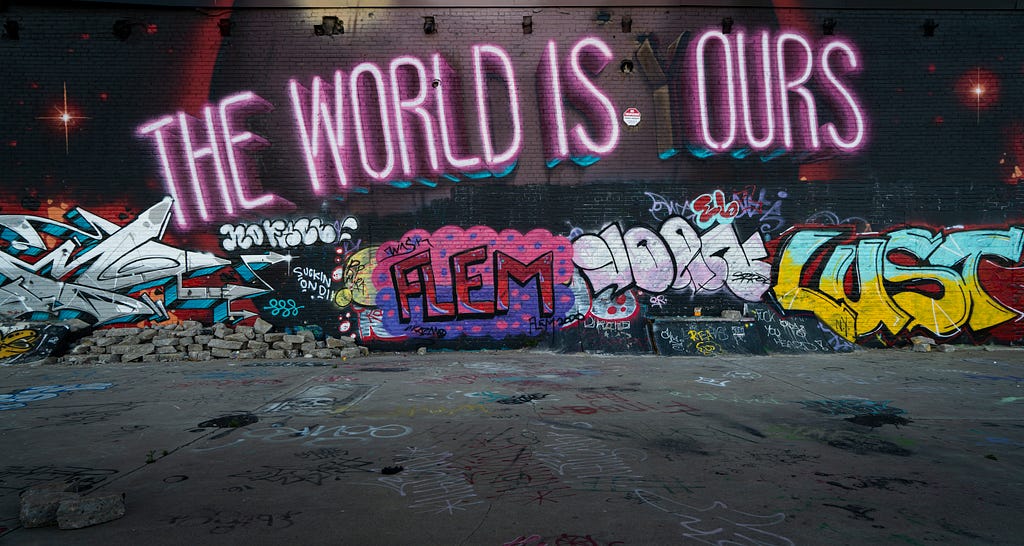 Graffiti on a black wall with a retro sign above it reading- The world is ours.