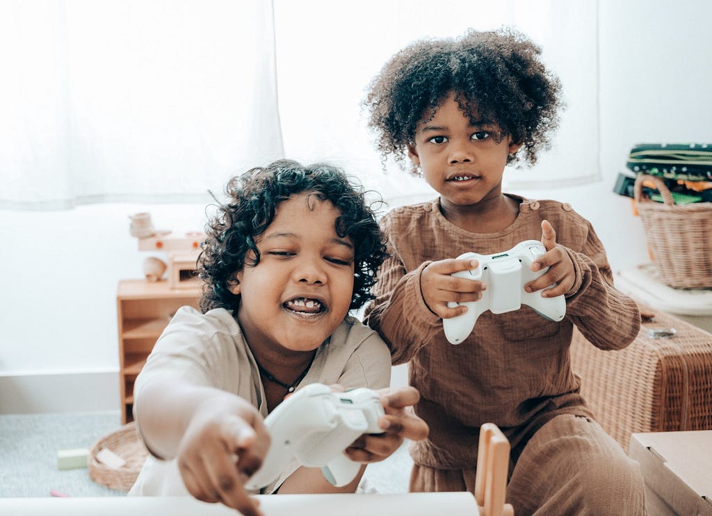 Duas crianças jogando videogame juntas, com controles brancos nas mãos. Ambas estão sorrindo e prestando atenção no jogo.