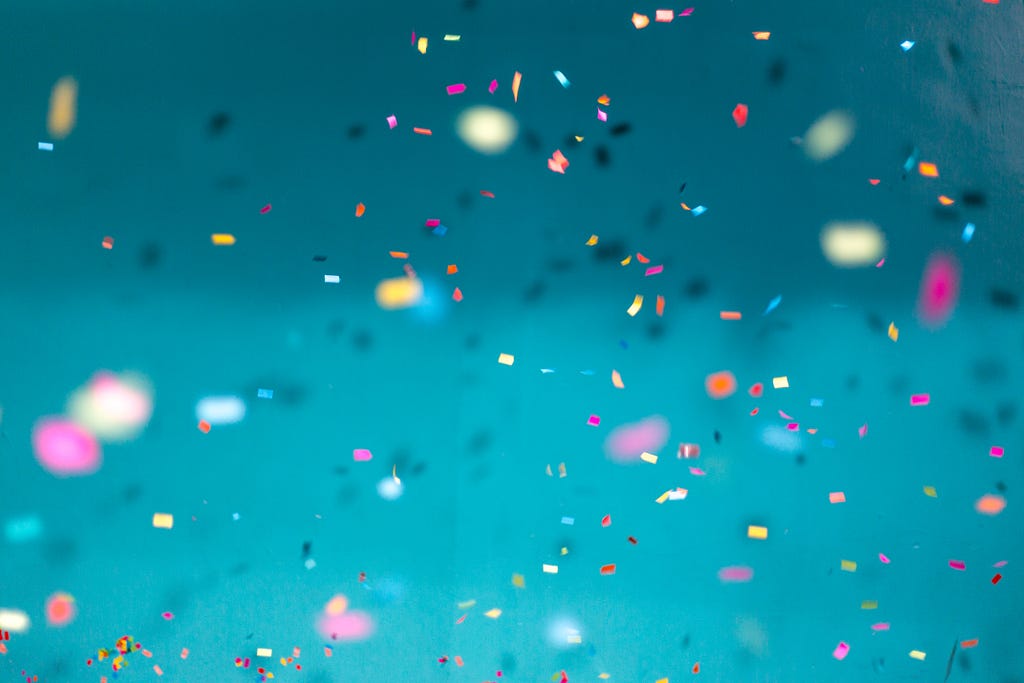 Colorful confetti falling on a blue background, with some pieces in focus and others blurred