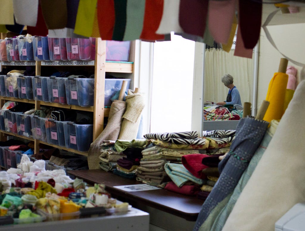 A mirror reflects Sally Briton as she sorts fabric, behind her a curtain blocks off the employee work area where employees compress bushels of clothing and fabric to send to Africa. Bailey Barnard / Klipsun Magazine