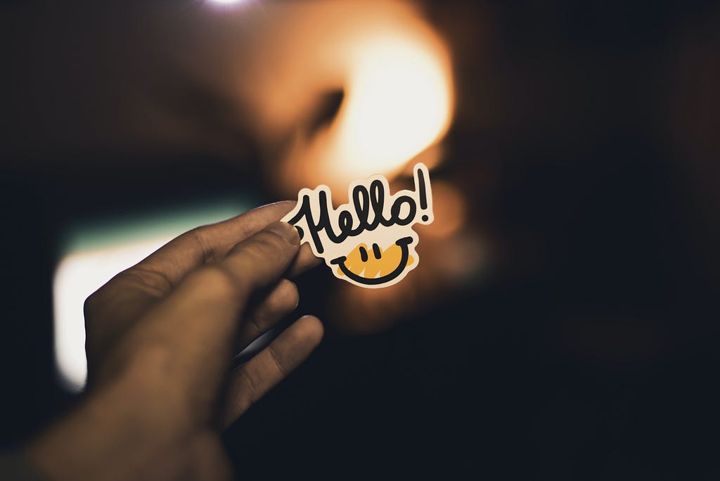 A hand holding an “hello” sticker up with light in the background.