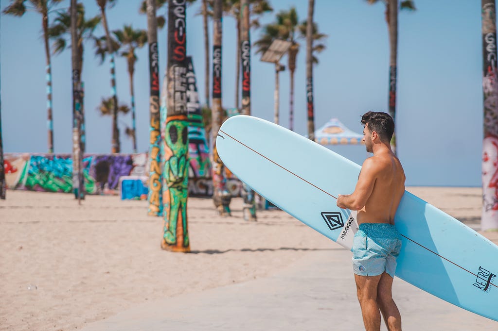 Man with surfboard on beach with graffiti