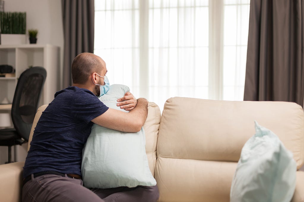 Man holding tight pillow sitting on couch during global pandemic.