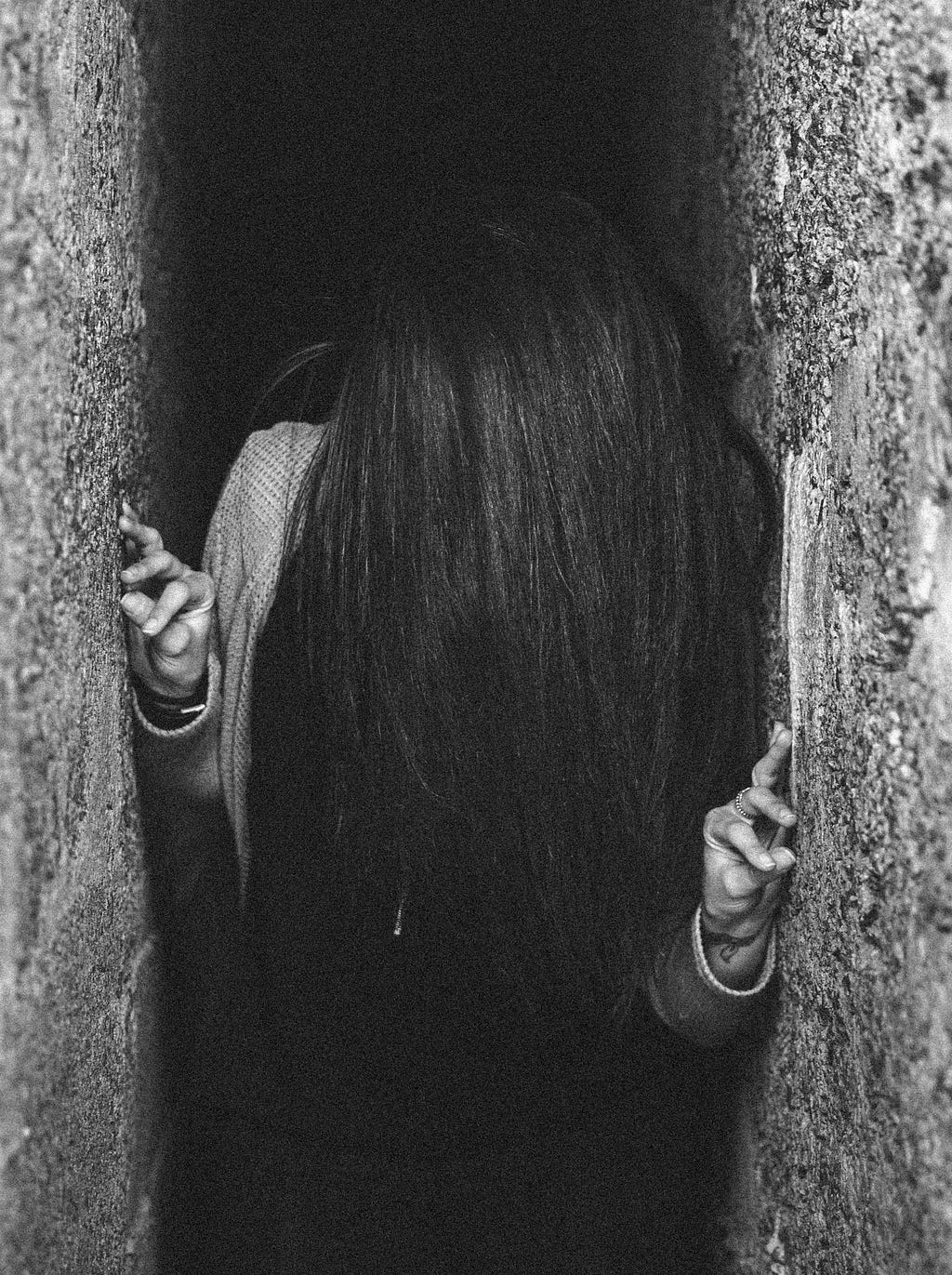 A young person with long black hair pushing against the walls of a narrow alleyway