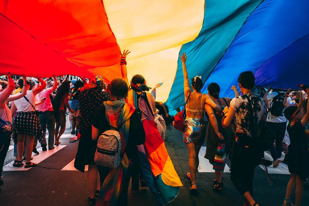 Pride march with large rainbow flag.