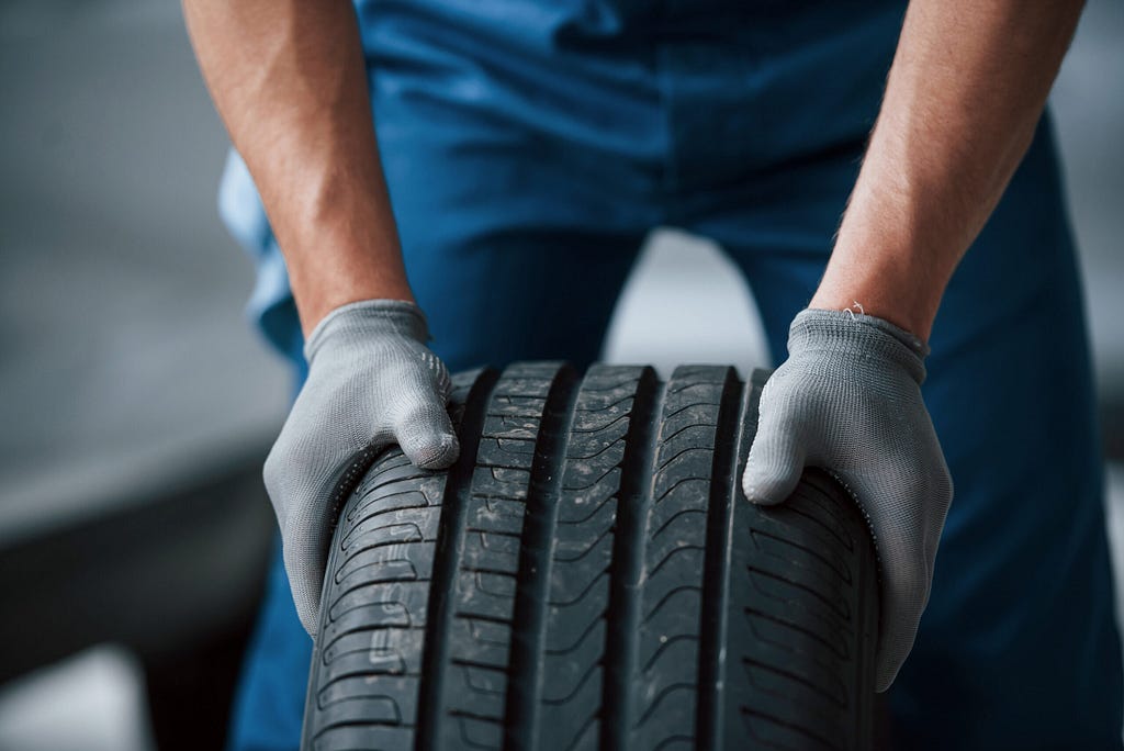 A mechanic, wearing a pair of gloves, holding a summer tire.