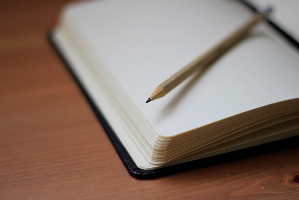 An empty notebook with a pencil resting on top, placed on a desk.