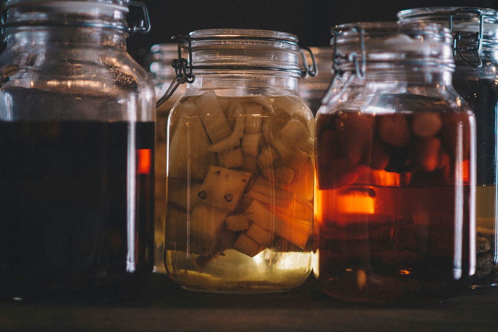 Jars of pickled vegetable with a dark background. Light is filtering through the jars with a warm tone.