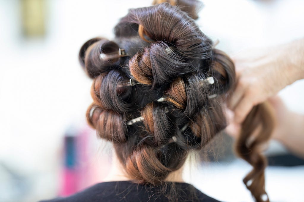 A woman being styled with big pin curls in a salon chair.