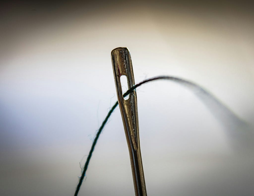 Closeup photo of the eye of a needle, with thread going through
