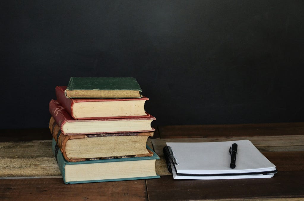 An image showing a collection of books bundled together, with a pen and a blank page placed beside them.