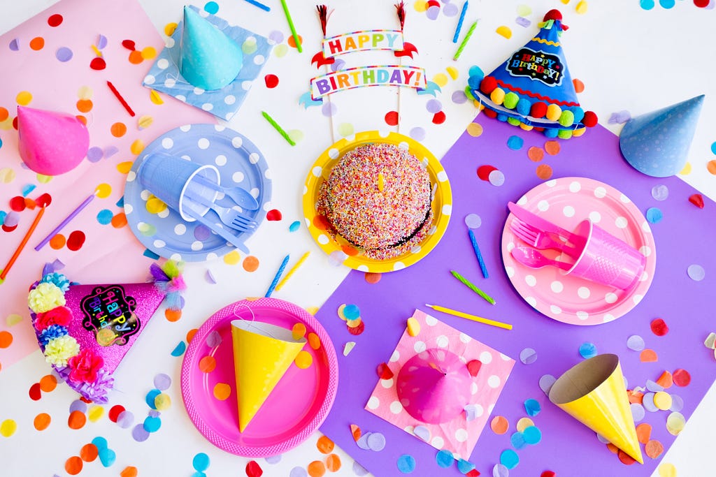 A birthday sign, cake, party hats, and confetti lay across a table
