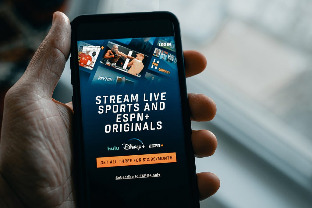 A smartphone is showing a package subscription page, with ESPN, Disney+ and HULU logo. The claim is : Stream live sports and ESPN+ Originals, with a monthly subscription at $12,99.