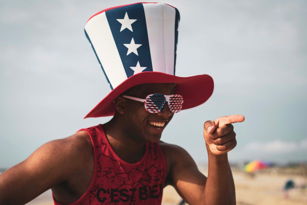 black man with a funny red white and blue hat on smiling and pointing