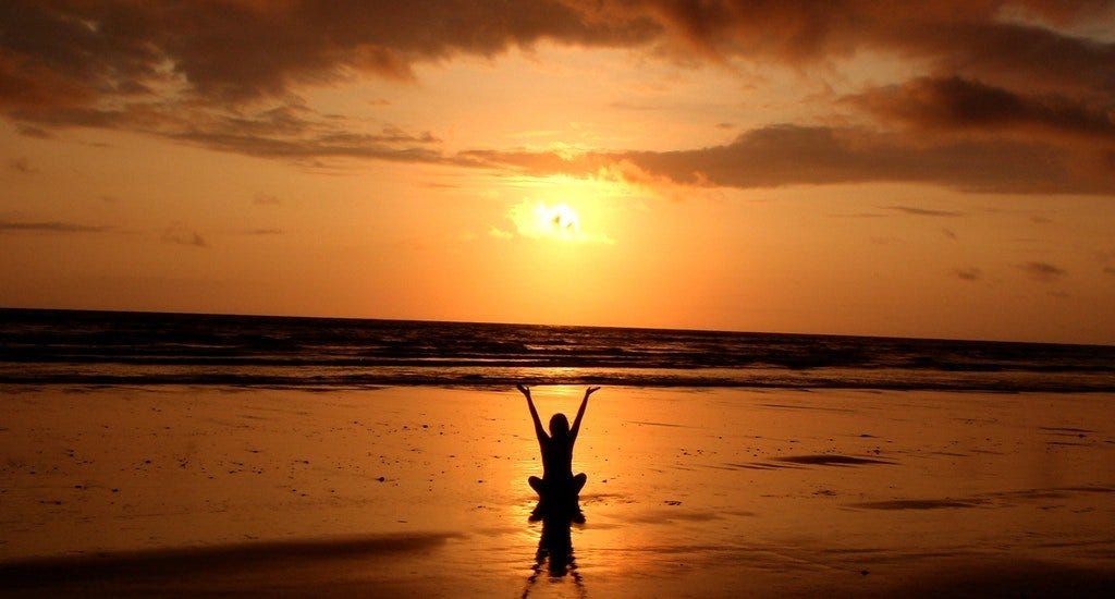 Person meditating on a beach during a sunset