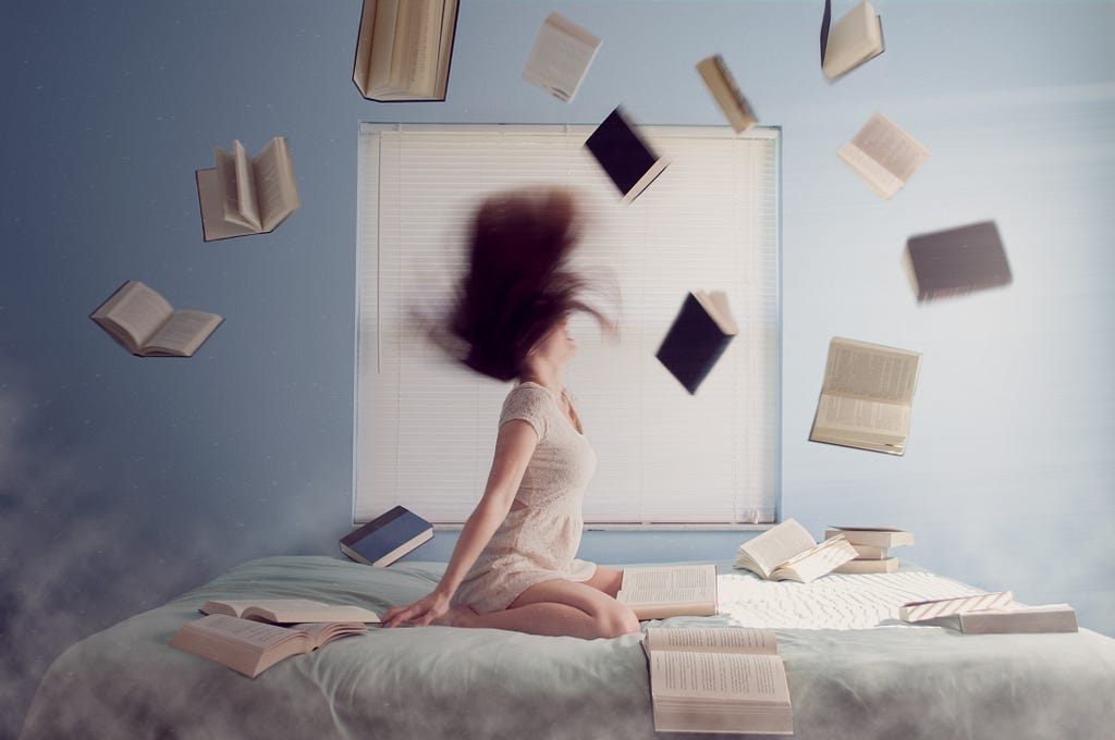 Eine weiblich gelesene Person, die auf einem Bett sitzt, während Bücher durch die Luft fliegen.