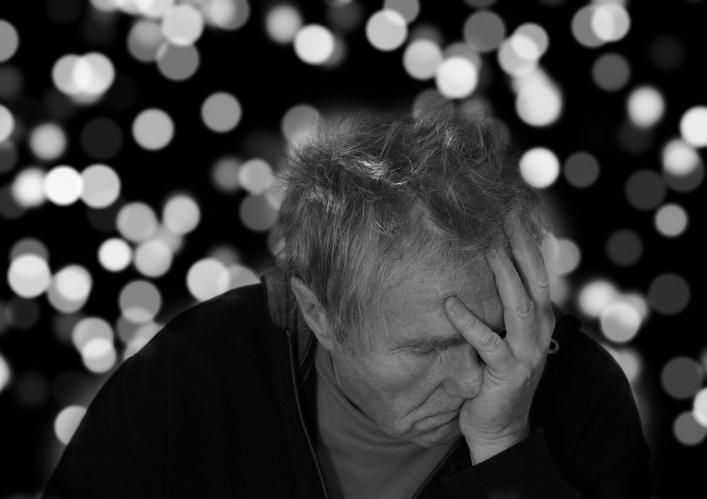 A black and white image of a man pushing his hand on his face displaying worry, forgetfulness or stress.