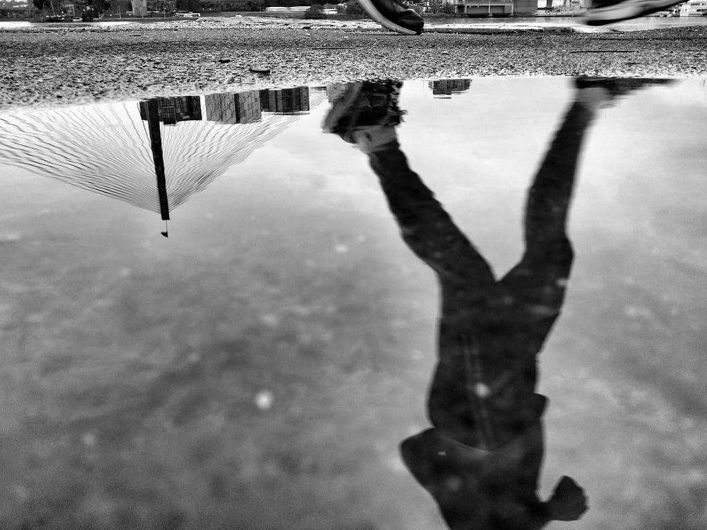 A runner outside reflected in a puddle.