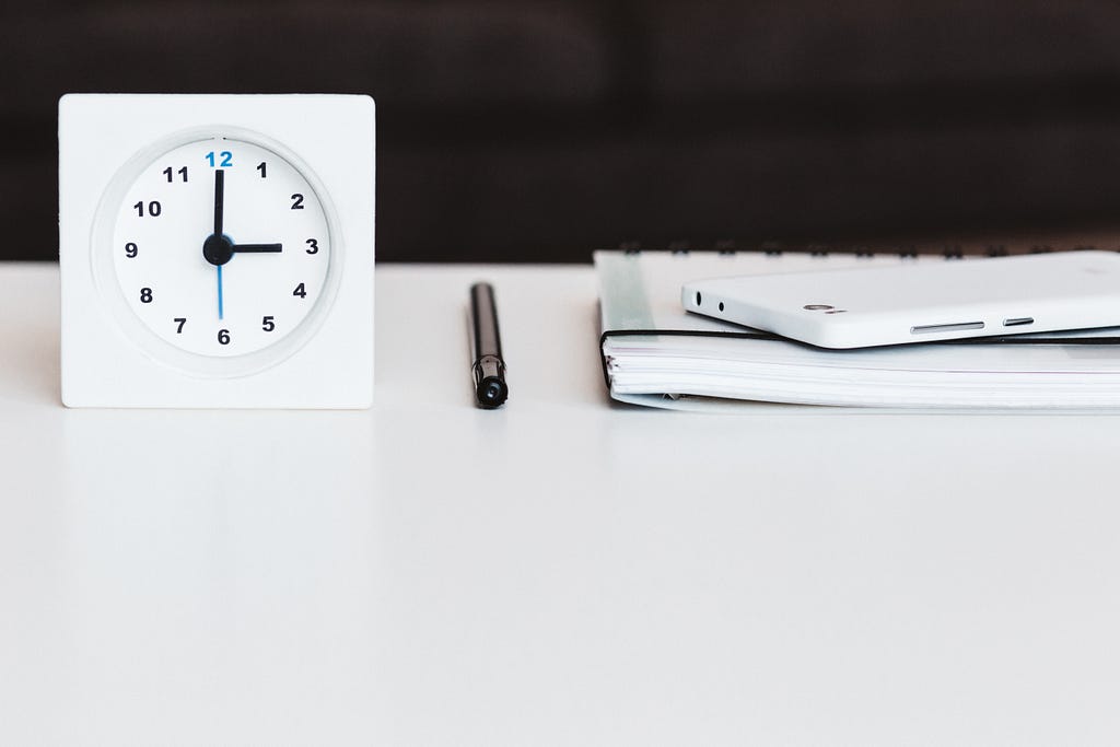 A clock and a notebook on a white work desk