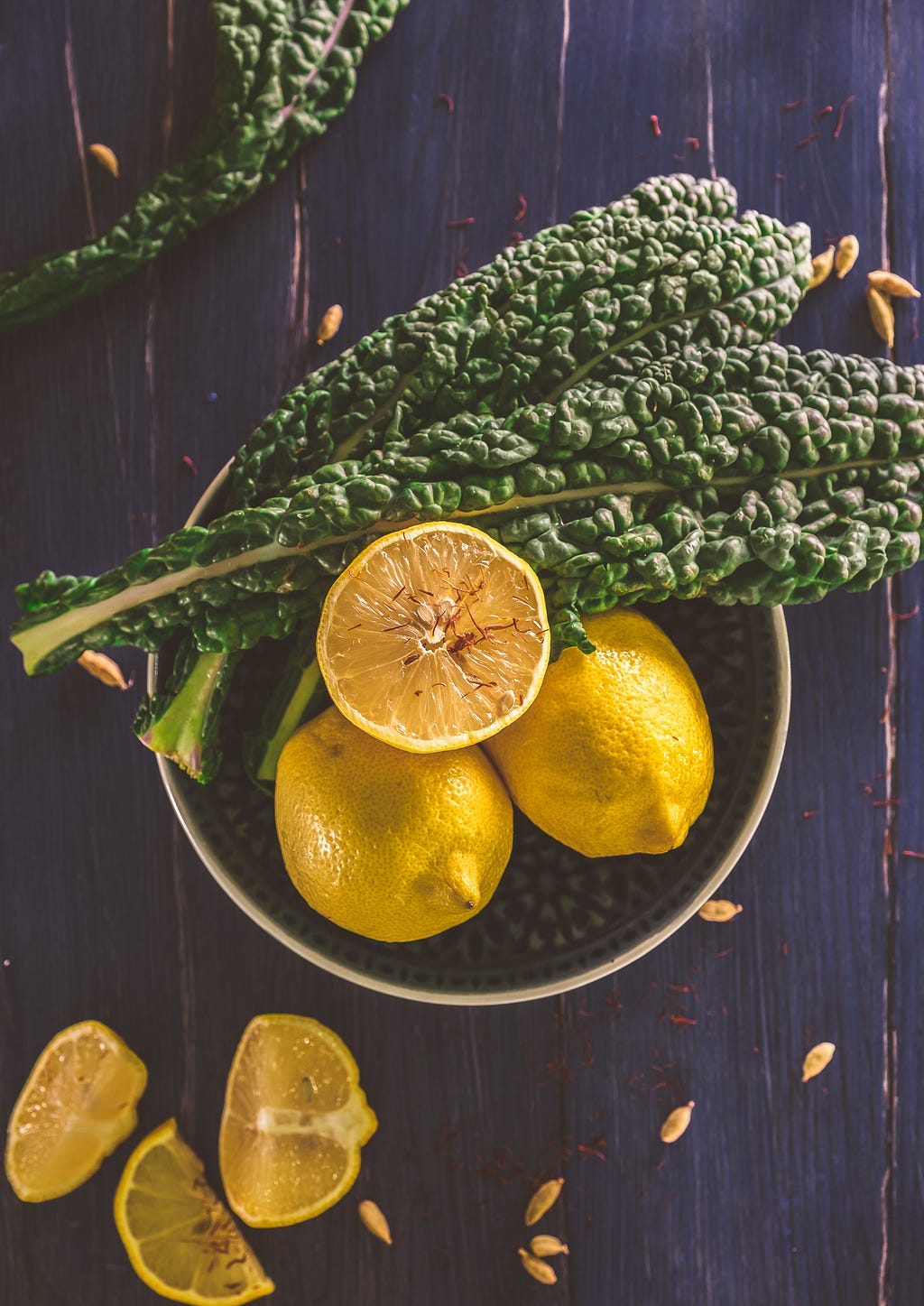 A decorative bowl full of fresh kale and lemons on a dark wooden table.