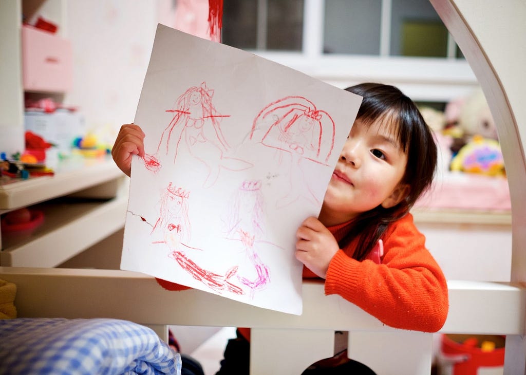Foto de uma criança em seu quarto segurando um papel com desenhos feitos por ela