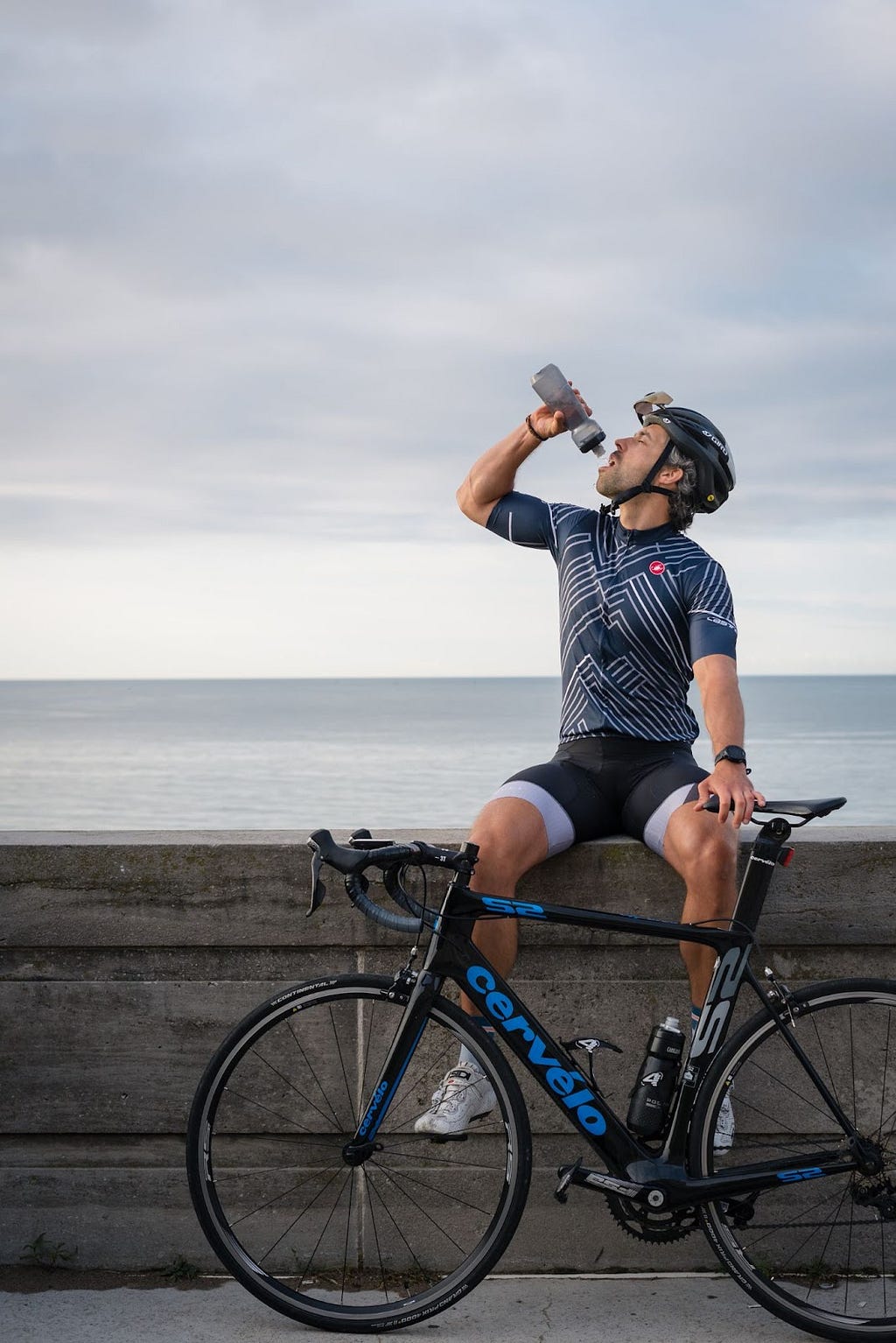 A cyclist drinking water while resting on a wall.