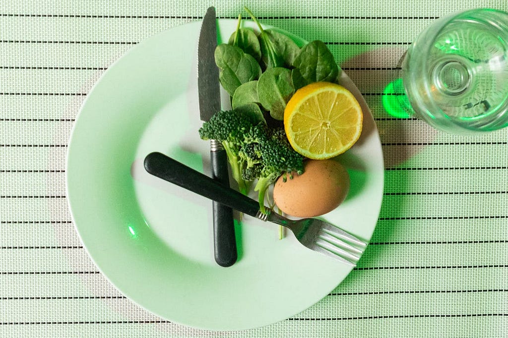 Spinach, lemon, broccoli, and egg on a plate.