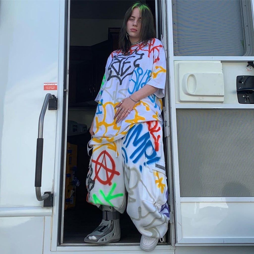 Eilish wearing an oversized white outfit covered in graffiti designs.