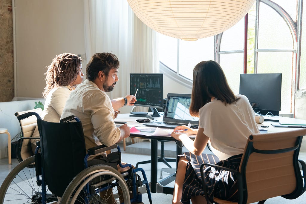 Three people, possibly team members, surrounding several computers and discussing something.