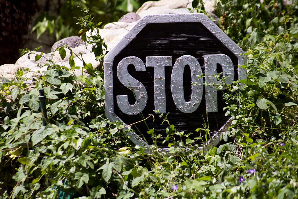 Wooden stop sign, sitting atop vines and bushes.
