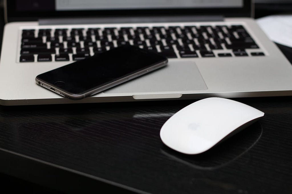 A wireless mouse next to a laptop with an iPhone resting on the keyboard