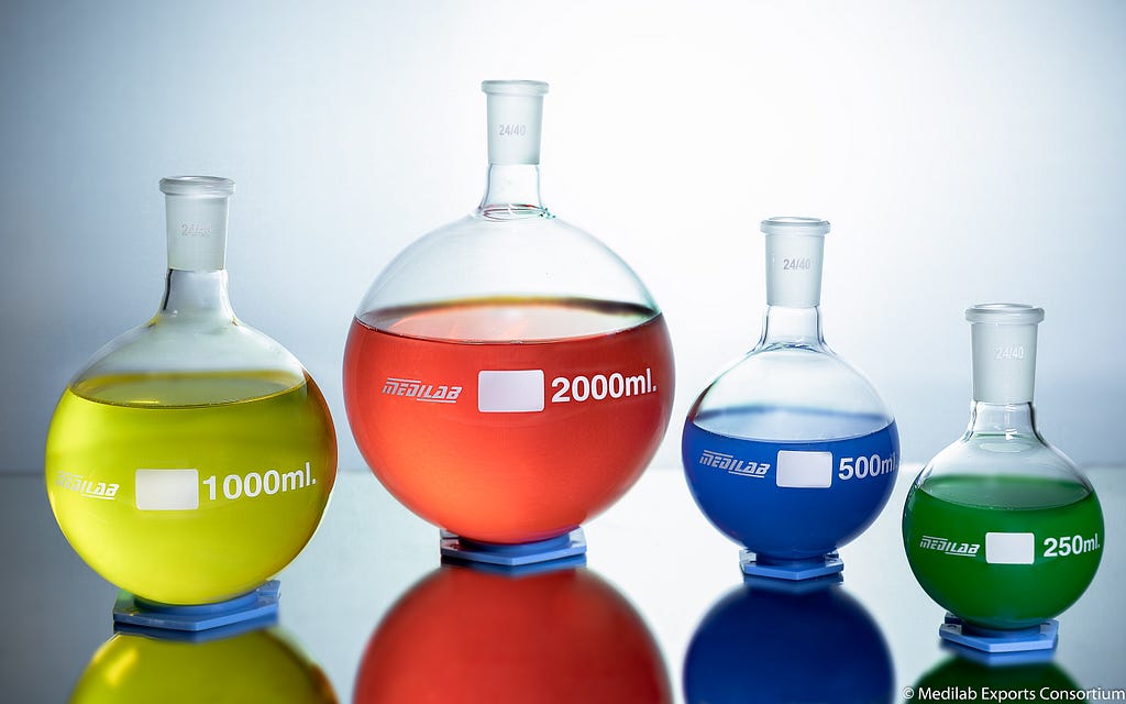 Round flasks filled with colorful liquids in yellow, red, blue, and green on a white, backlit background