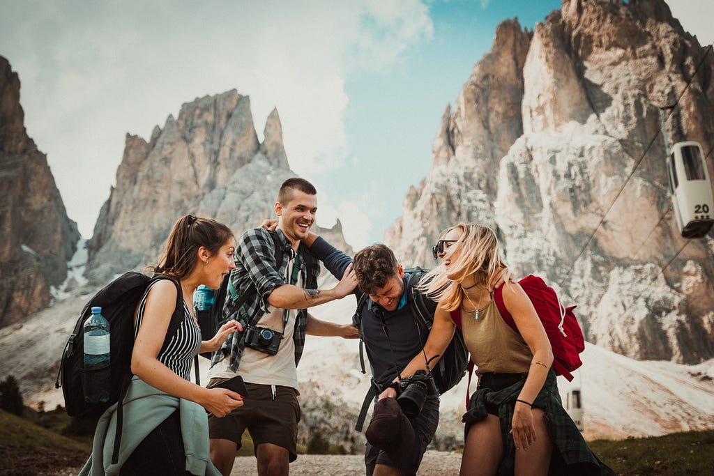 Four friends in hiking gear in front of a rocky cliff thing.