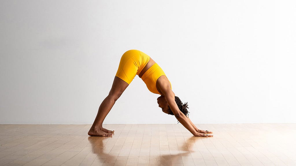 A black woman in yellow yoga attire doing the “downward dog yoga pose”