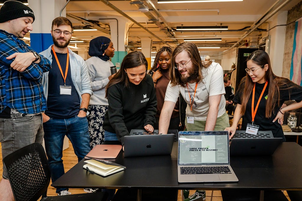 Group of Makers stand around table discussing what is on a laptop screen