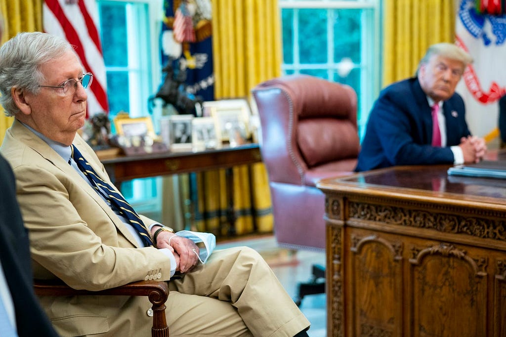 Senate Majority Leader Mitch McConnell listens to President Donald Trump talk to reporters in the Oval Office.