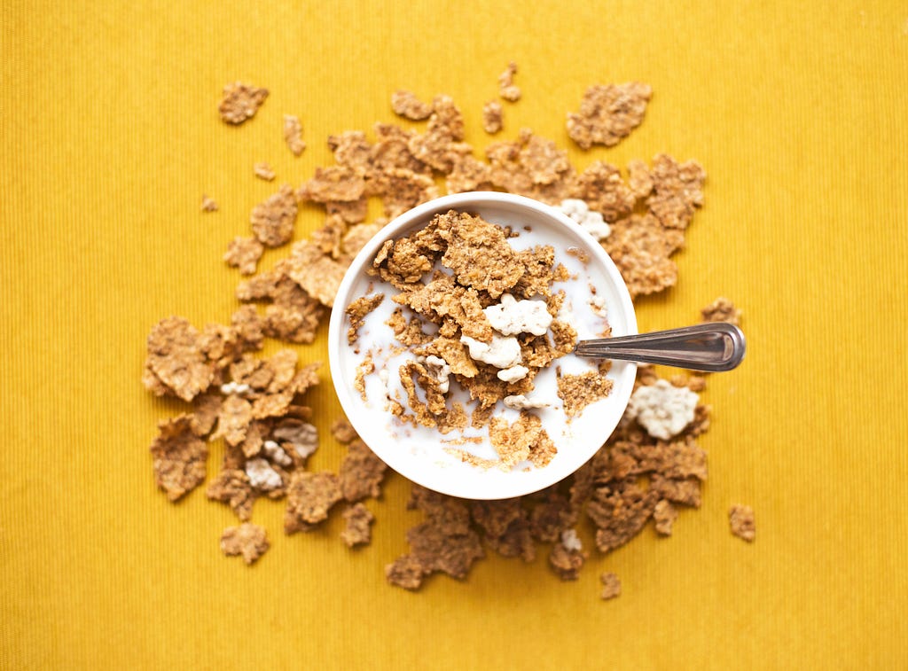 A bowl of cereal on a yellow background. A lot of cereal is on the table.