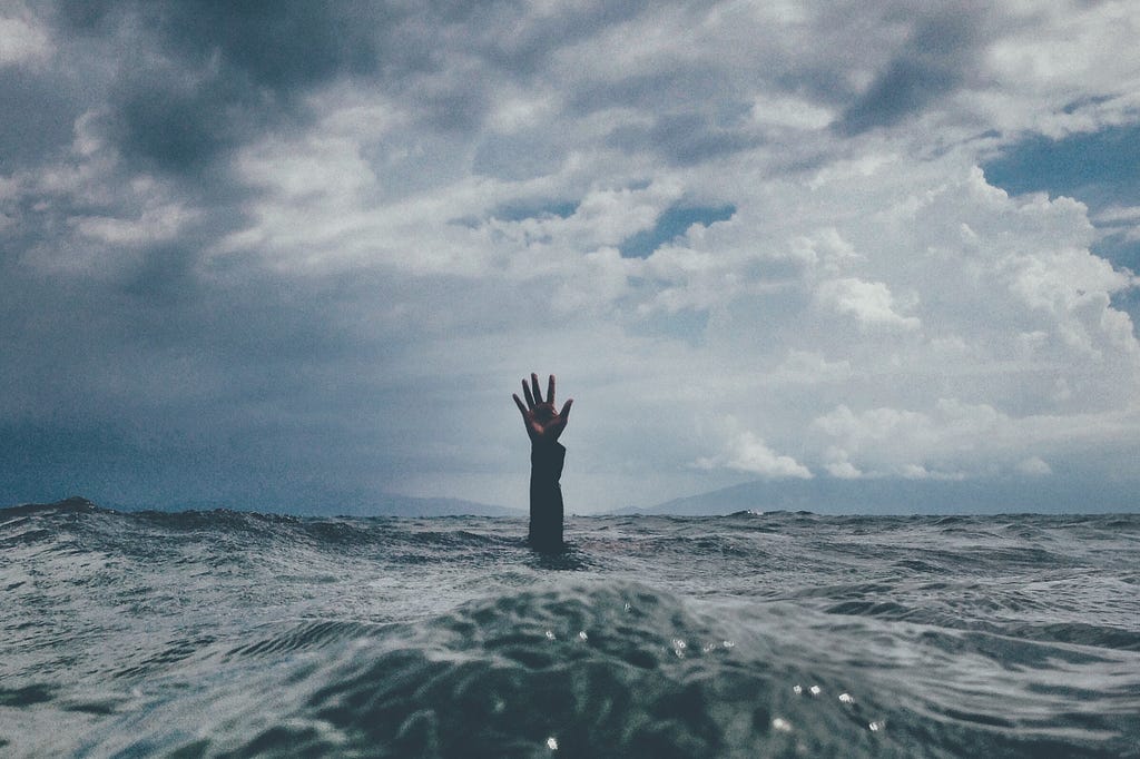 Someone reaching up to the sky as they sink lower below the waves of the ocean. Drowning.