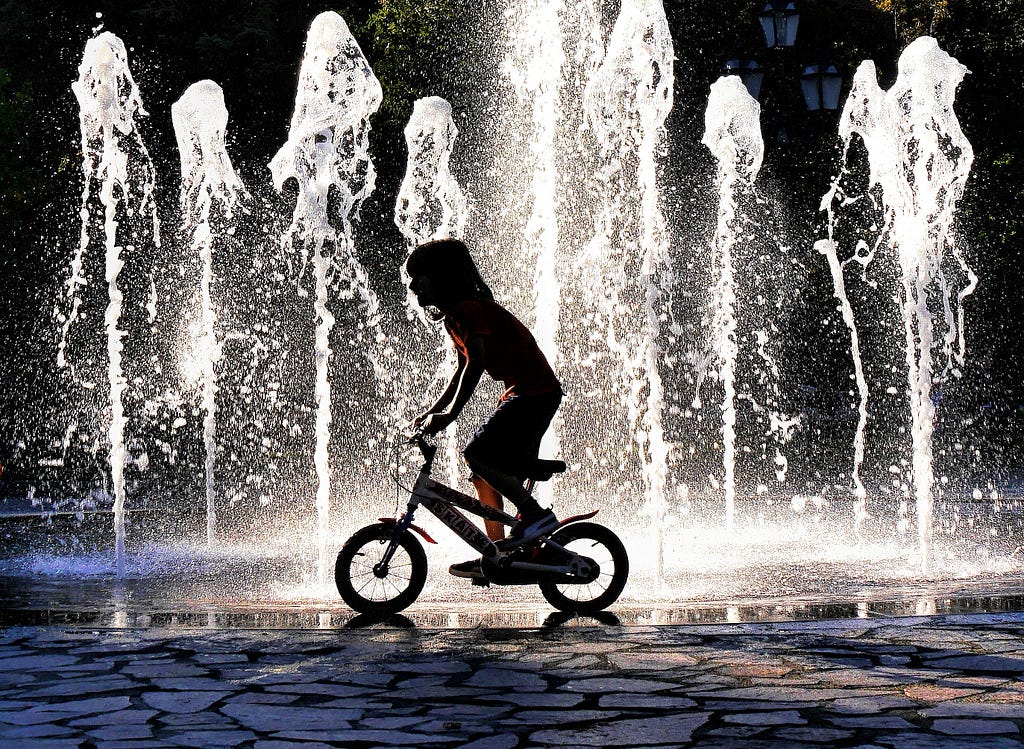 A young child riding their bmx bike while jets of water shoot up around them