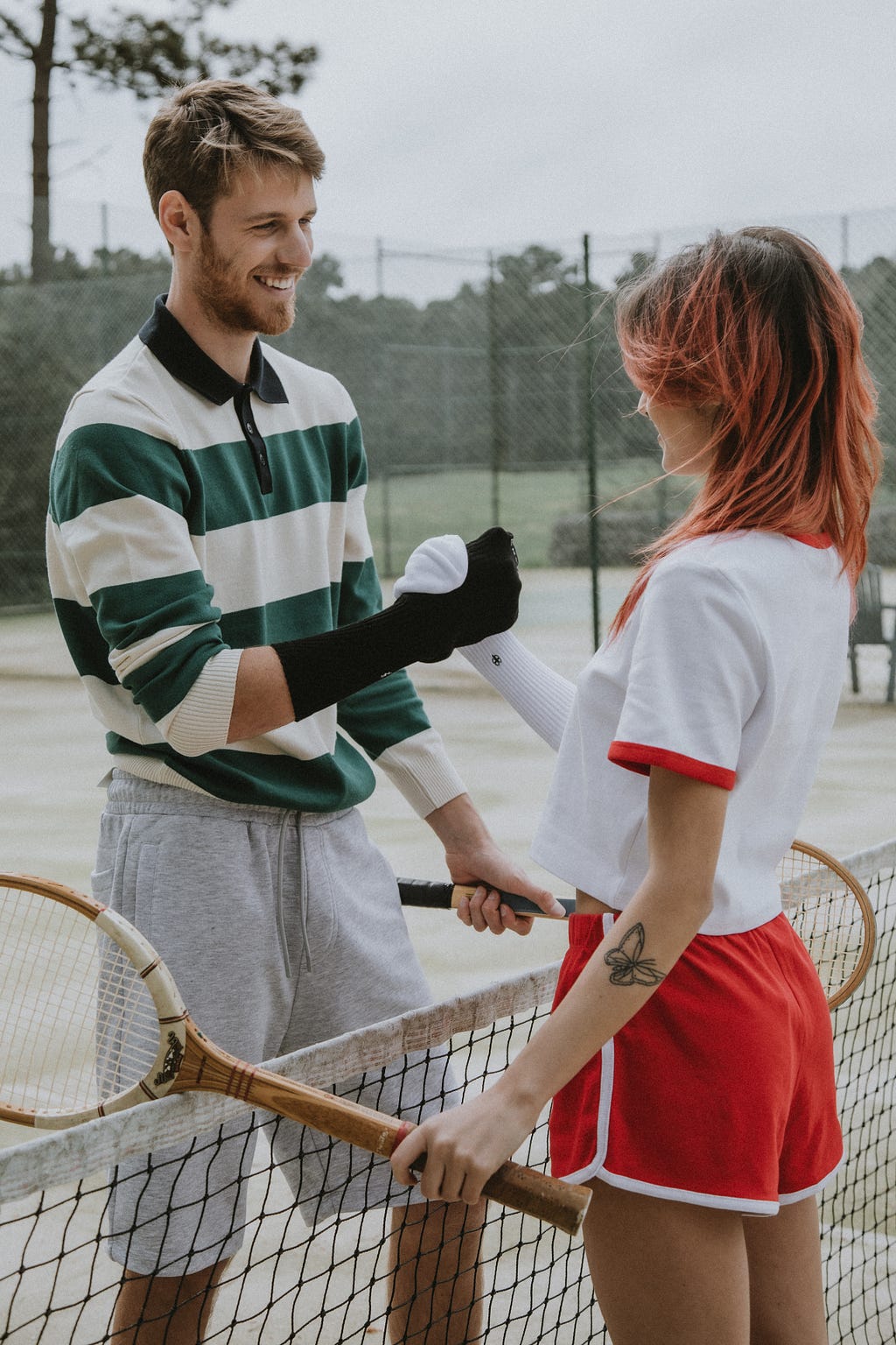Two Lawn Tennis opponents, a male, and a female, shake their hands at the net.