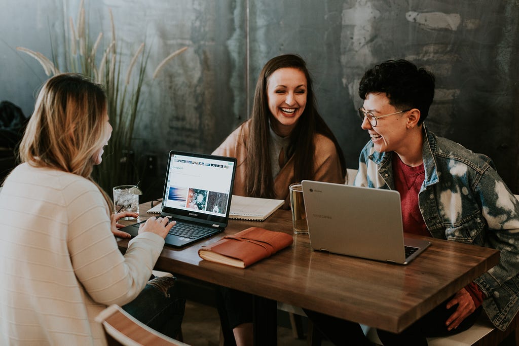 Three people at a table with their laptops smiling and having a conversation