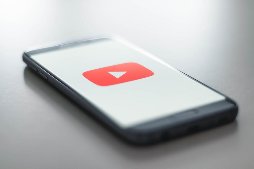 Cellphone lying on a neutral-colored surface, the red YouTube logo filling the white screen
