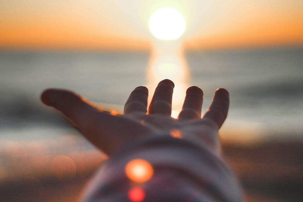 A hand reaching out to the sun