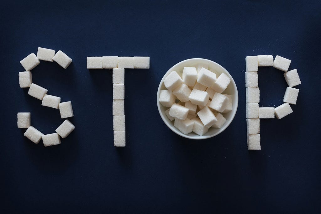 An image of a the letters ‘S-T-O-P’ with the a bowl full of cubed sugar in between the word, STOP.