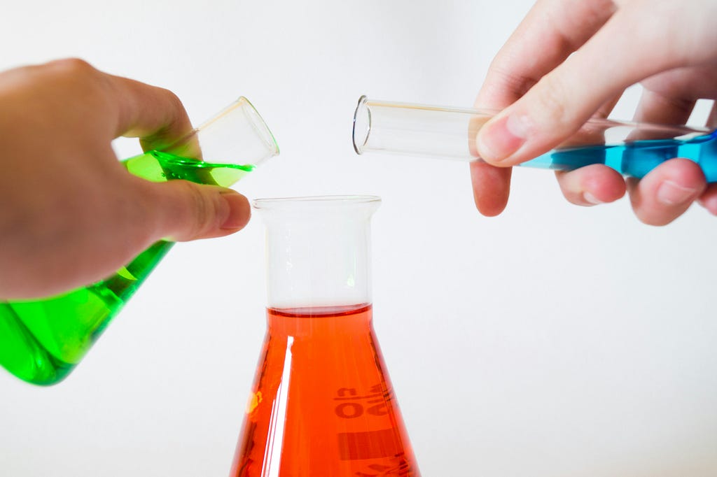Beakers of different coloured liquid are poured into another beaker to represent science.