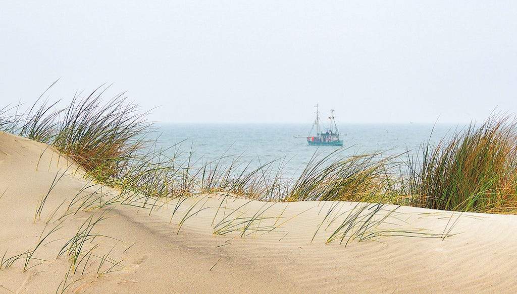 fishing boat at the North Sea,  seen from sandy dunes