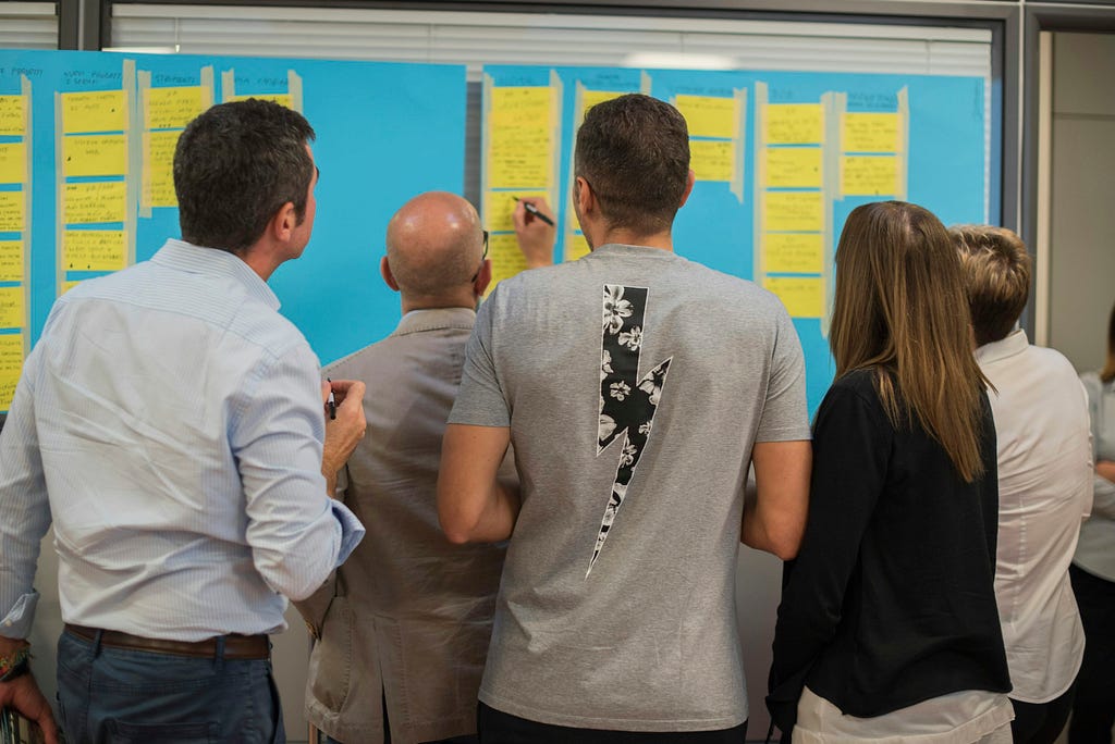 People standing around a whiteboard with sticky-notes on it, looking busy