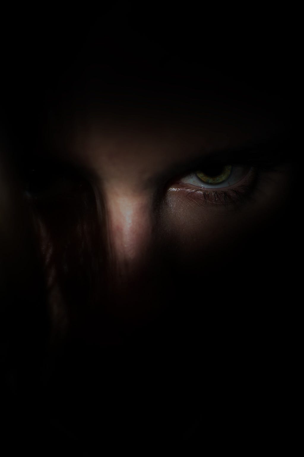 A man in darkness trying to find some light, whose eyes are evident in the dark.