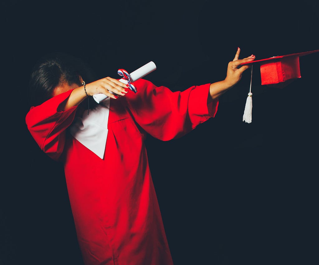 A person in a red graduation gown dabbing with a diploma and cap in their hands.